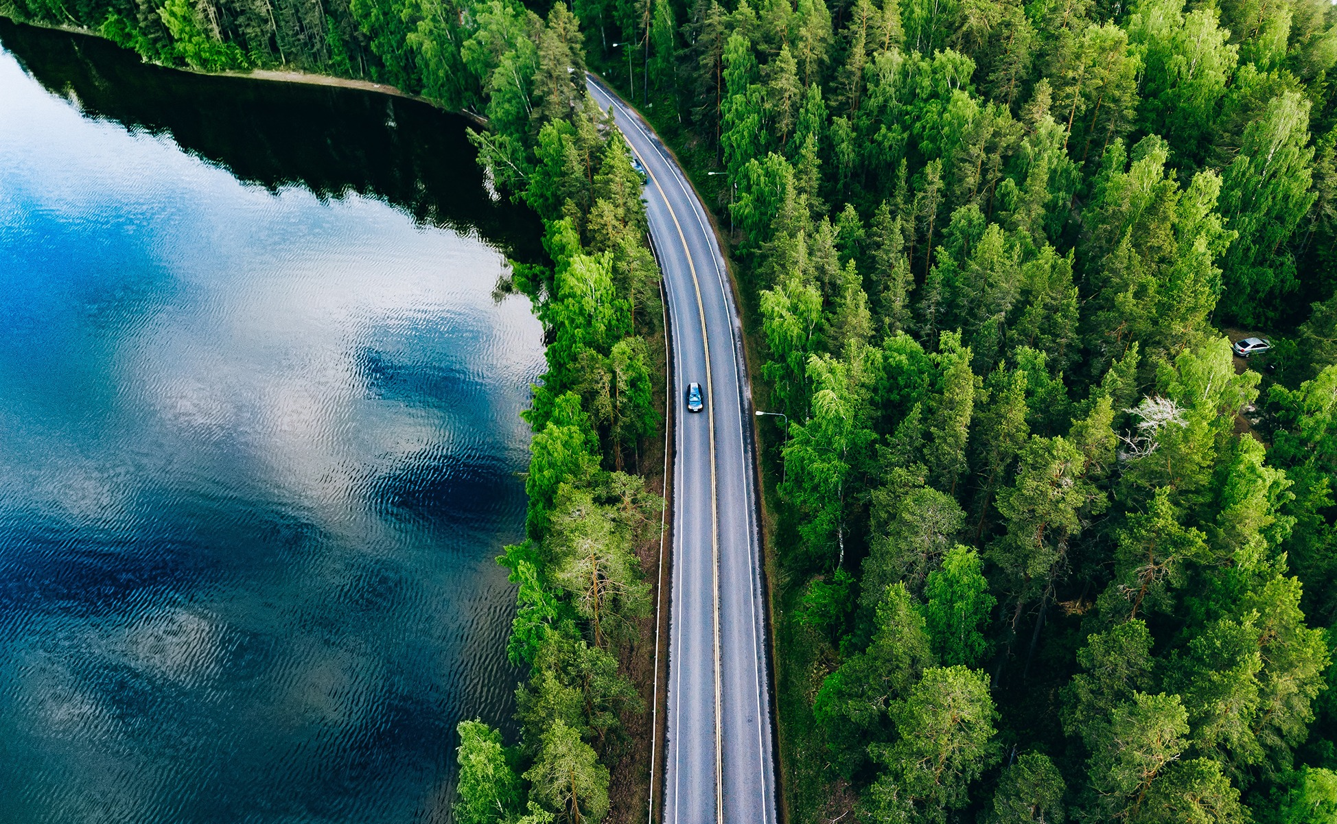 Samochód jadący drogą między jeziorem a lasem